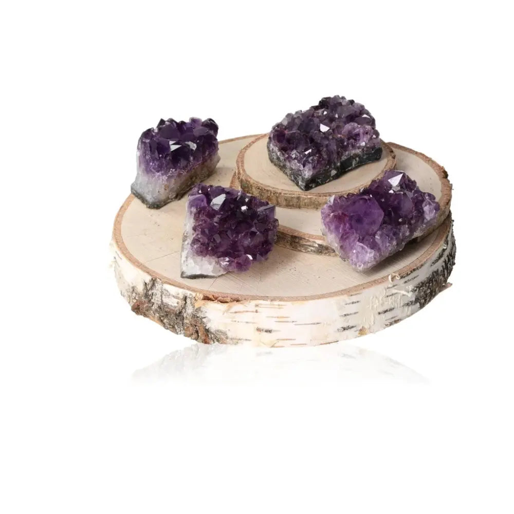 Four Amethyst Druze crystals on a wooden round display, showcasing their vibrant purple hues and sparkling formations.