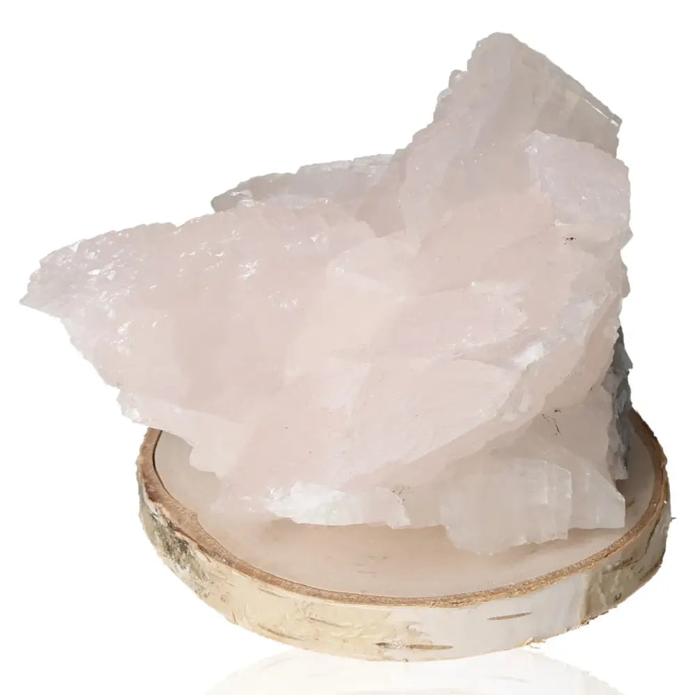 Soft pink Manganocalcite gemstone displayed on a wooden base, symbolizing emotional healing and forgiveness.