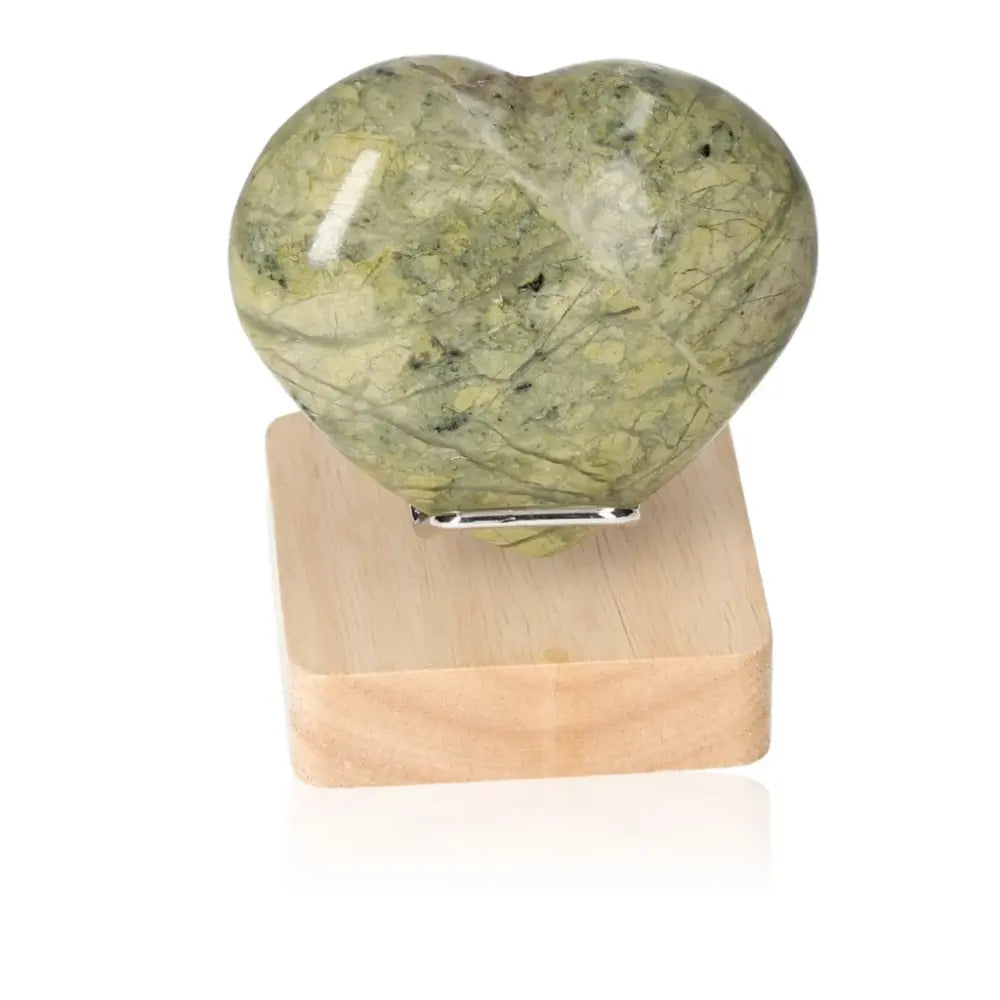 Heart-shaped Serpentine crystal on wooden stand, symbolizing healing energies and spiritual wisdom.