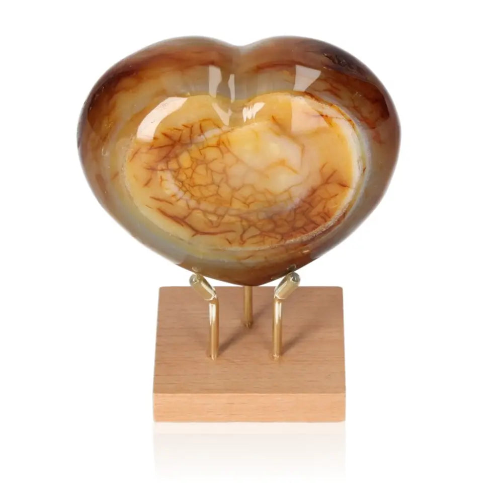 Carnelian heart gemstone with rich orange-red hues on wooden stand, symbolizing passion and vitality.