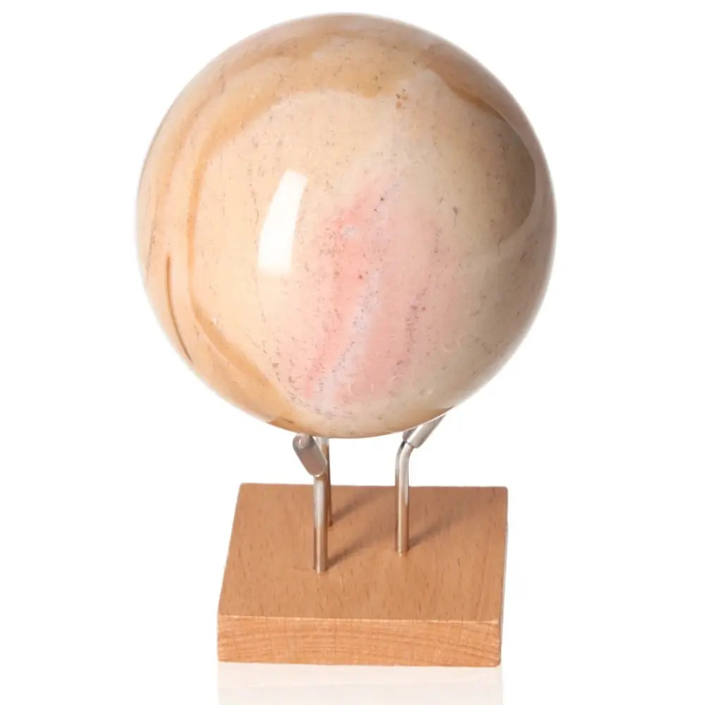 Peach Moonstone sphere with soothing peach and pink hues on a wooden stand, symbolizing calm and emotional healing.