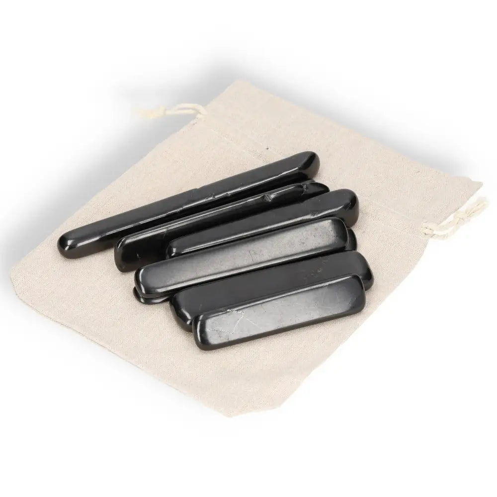 Shungite Tumbled Sticks M displayed on a beige fabric pouch, showcasing smooth black surfaces and healing properties.