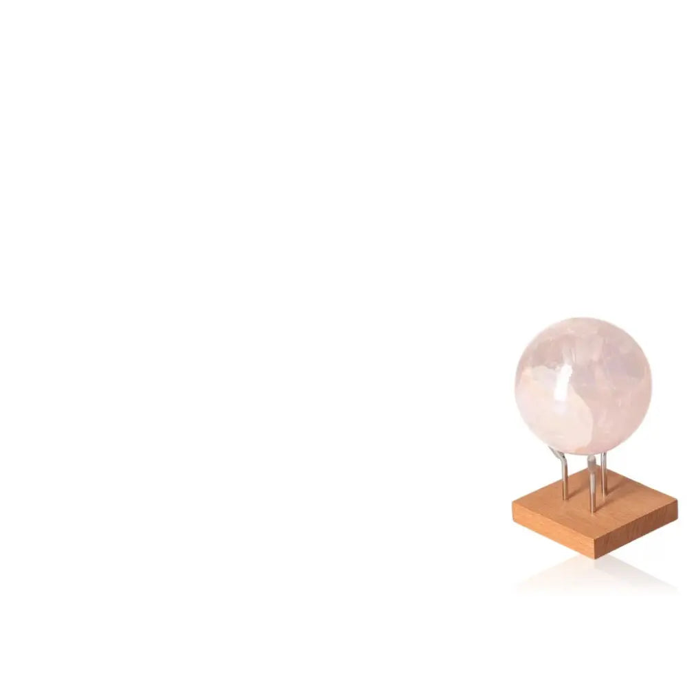 Sylvia Crystals' Pink Quartz Sphere on wooden stand, symbolizing love, elegance, and spiritual connection; crafted from natural, ethical quartz.
