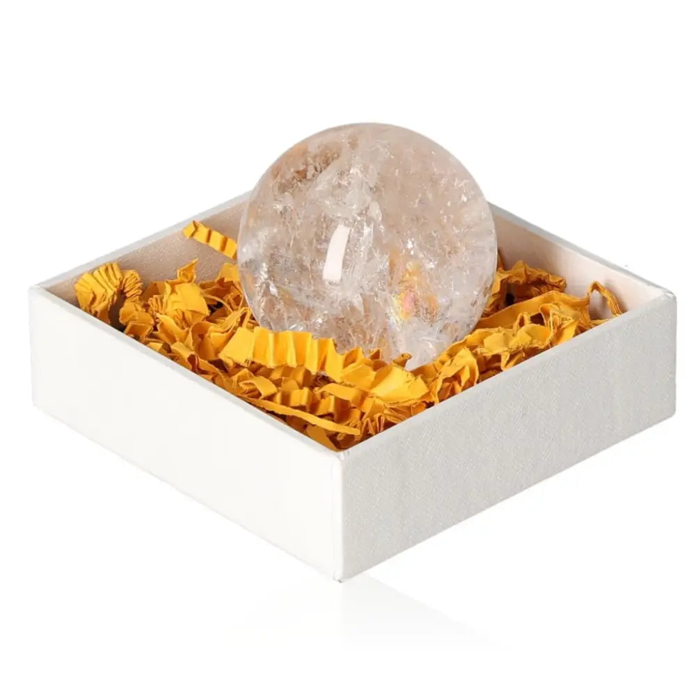 Lemurian Quartz Sphere in a white box with yellow crinkle paper, highlighting its serene aura and purification properties.