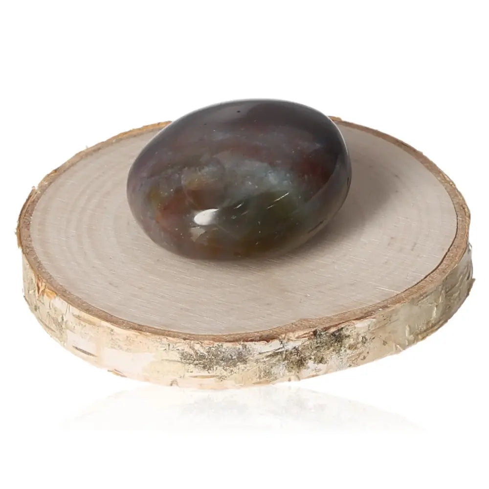 Tumbled Grenatite bloodstone with distinctive red spots on wooden stand, enhancing vitality and promoting courage and resilience.