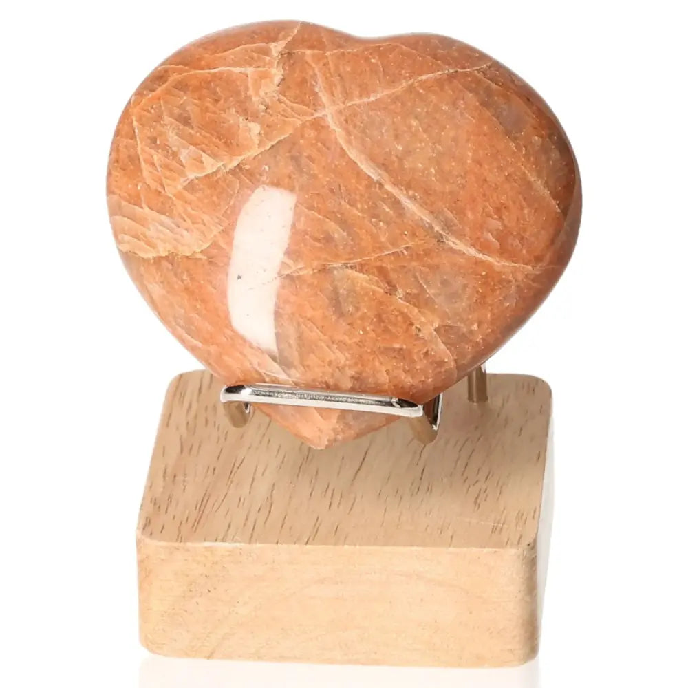 Peach Moonstone Heart promoting emotional balance and intuition, displayed on a wooden stand. Enhances sensitivity and protects against nightmares.