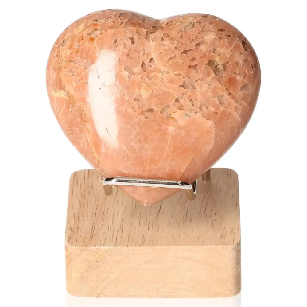 Peach Moonstone Heart crystal on wooden stand, enhances emotional balance and intuition, promotes restful sleep.