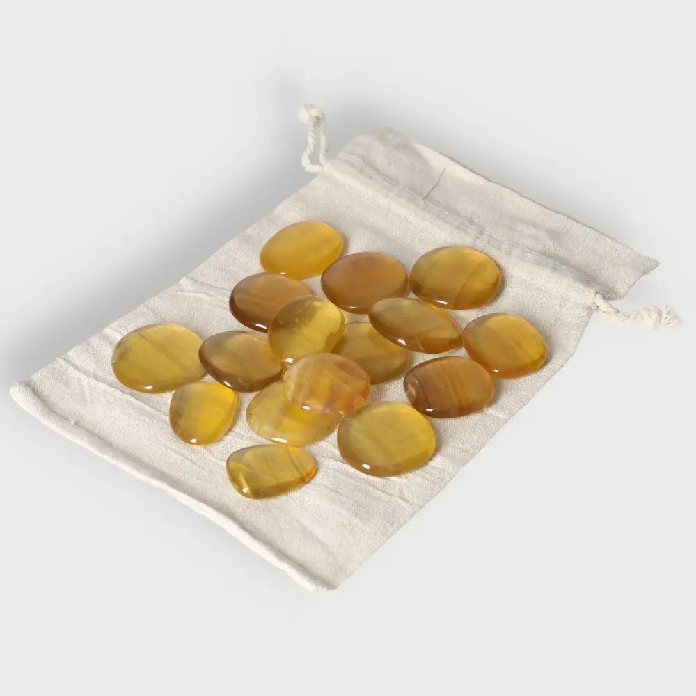 Golden fluorite palm stones on a white drawstring pouch, ideal for enhancing creativity, learning, and professional development.