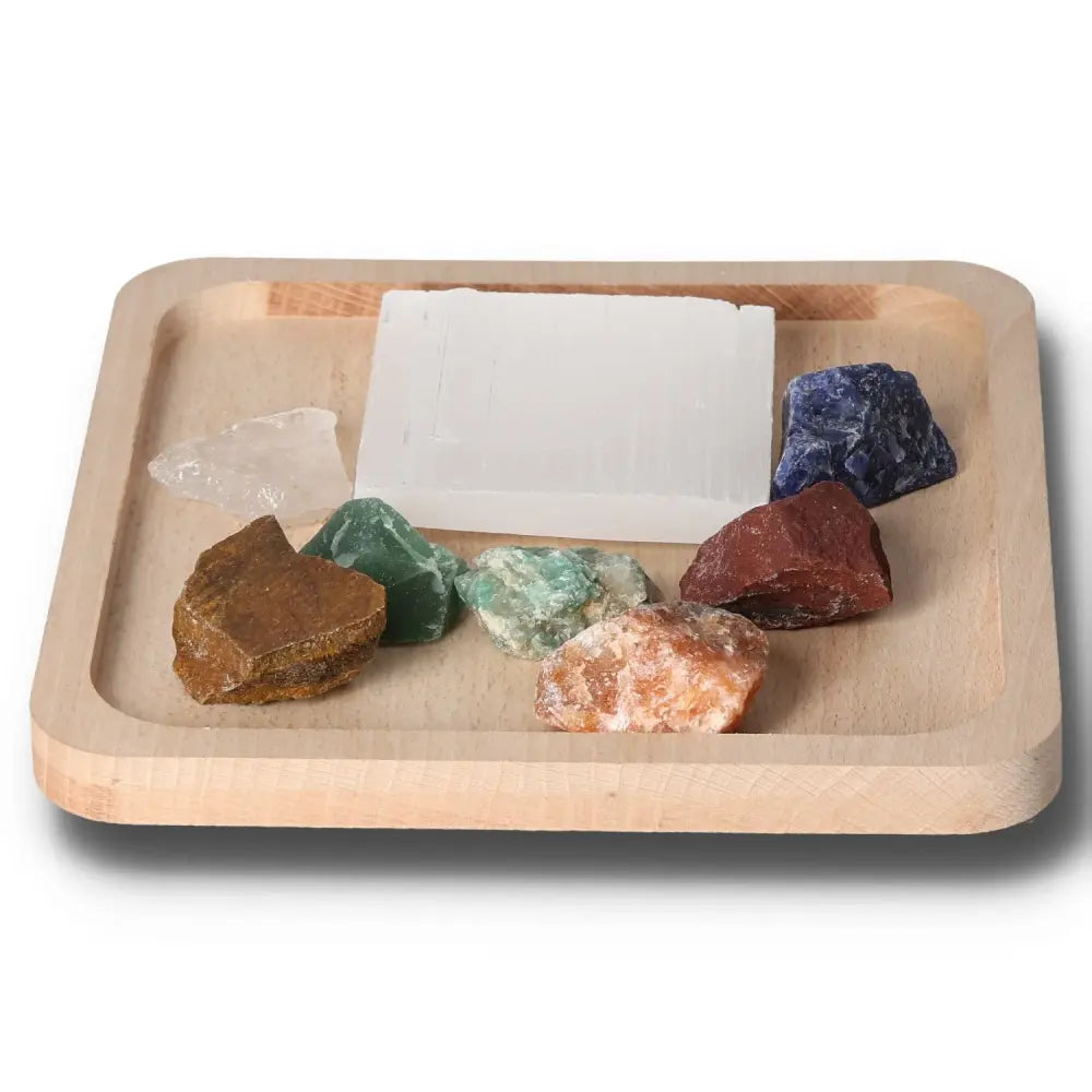 Set of 7 chakra stones with selenite charging plate for energy alignment on a wooden tray.