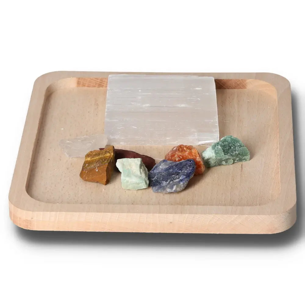 Chakra stones set with selenite charging plate, featuring seven colored stones for energy alignment on a wooden tray.
