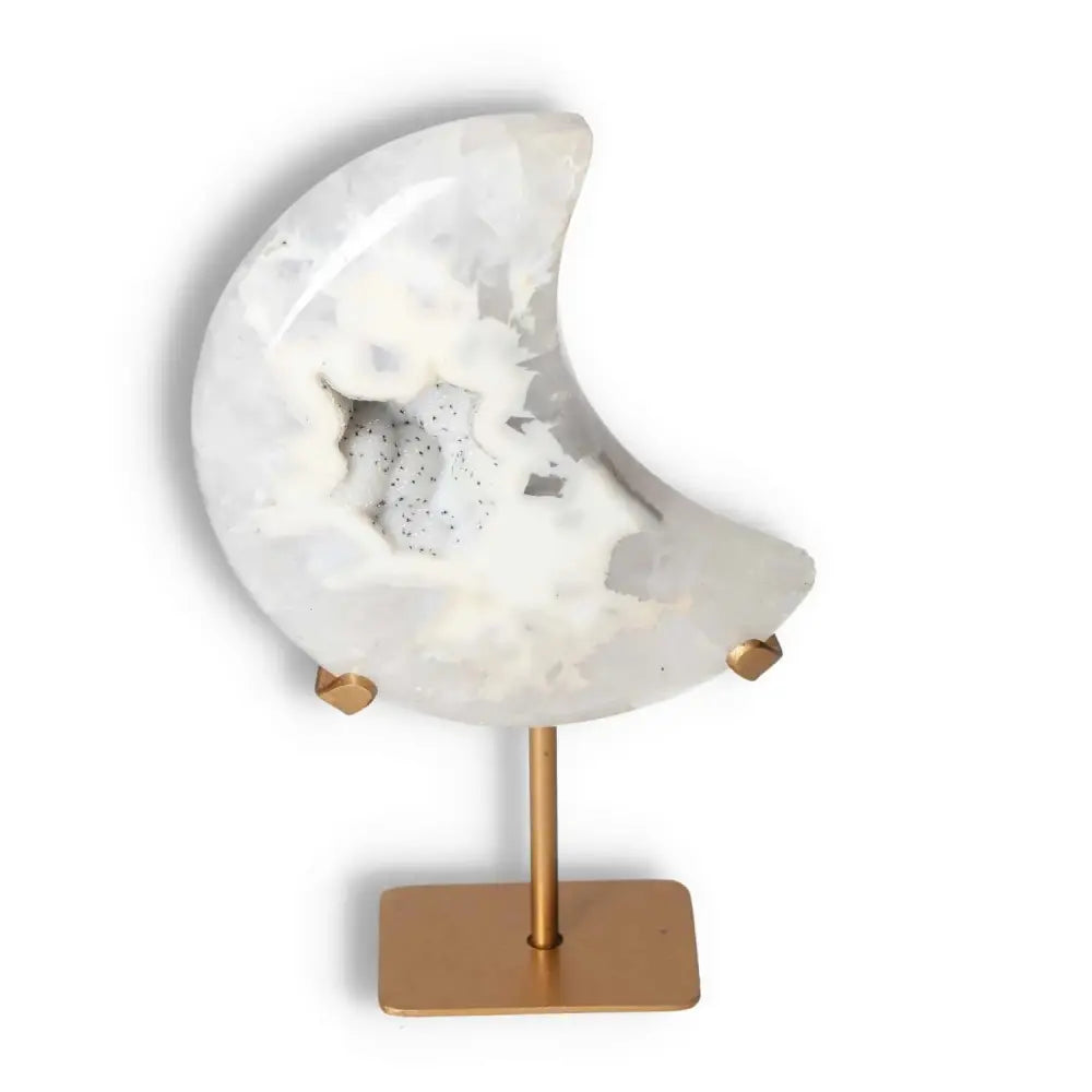 Agate lunar crescent sculpture with geode center on a gold stand, showcasing soft off-white and delicate hues.