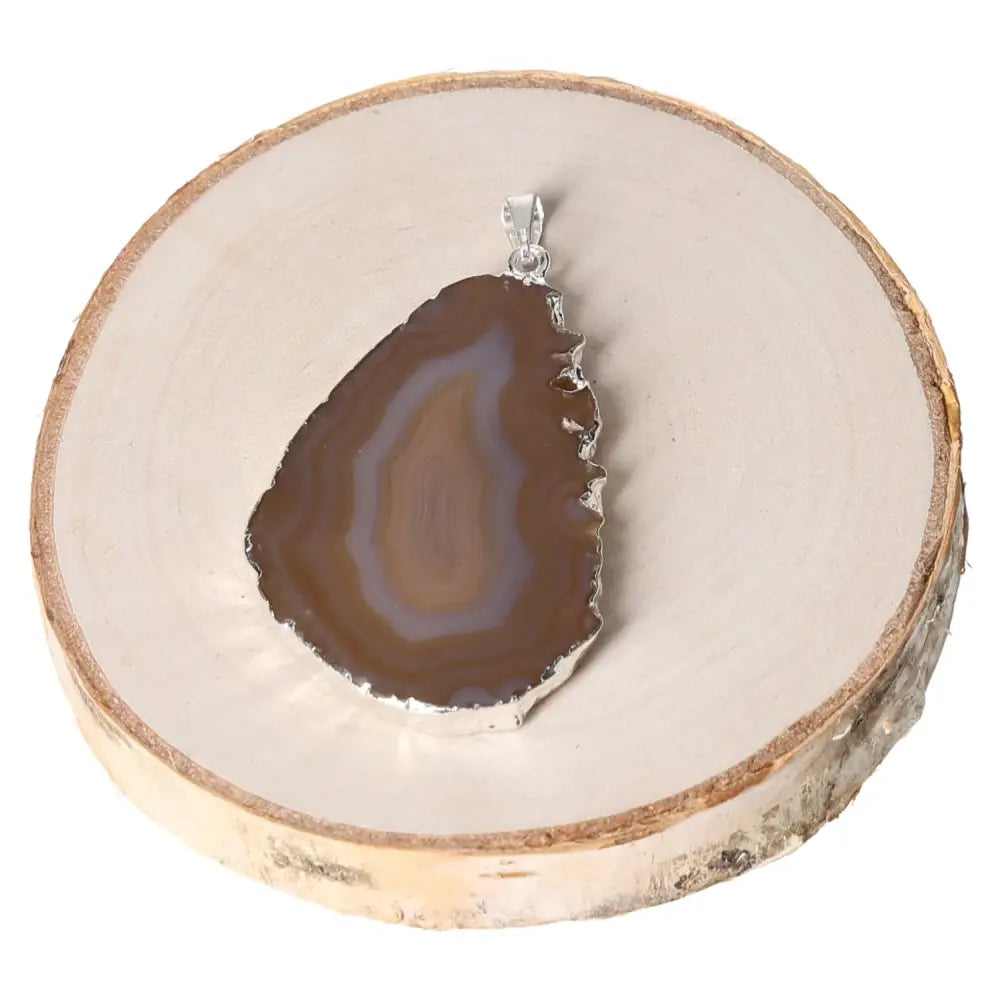 Elegant agate slice pendant with natural banding patterns and metal plating on a wooden display.