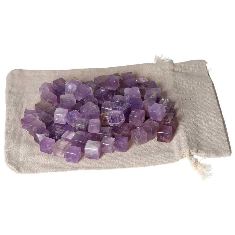 Amethyst small cubes spread on a beige cloth, known for stress relief and energy boost, enhancing concentration and emotional stability.