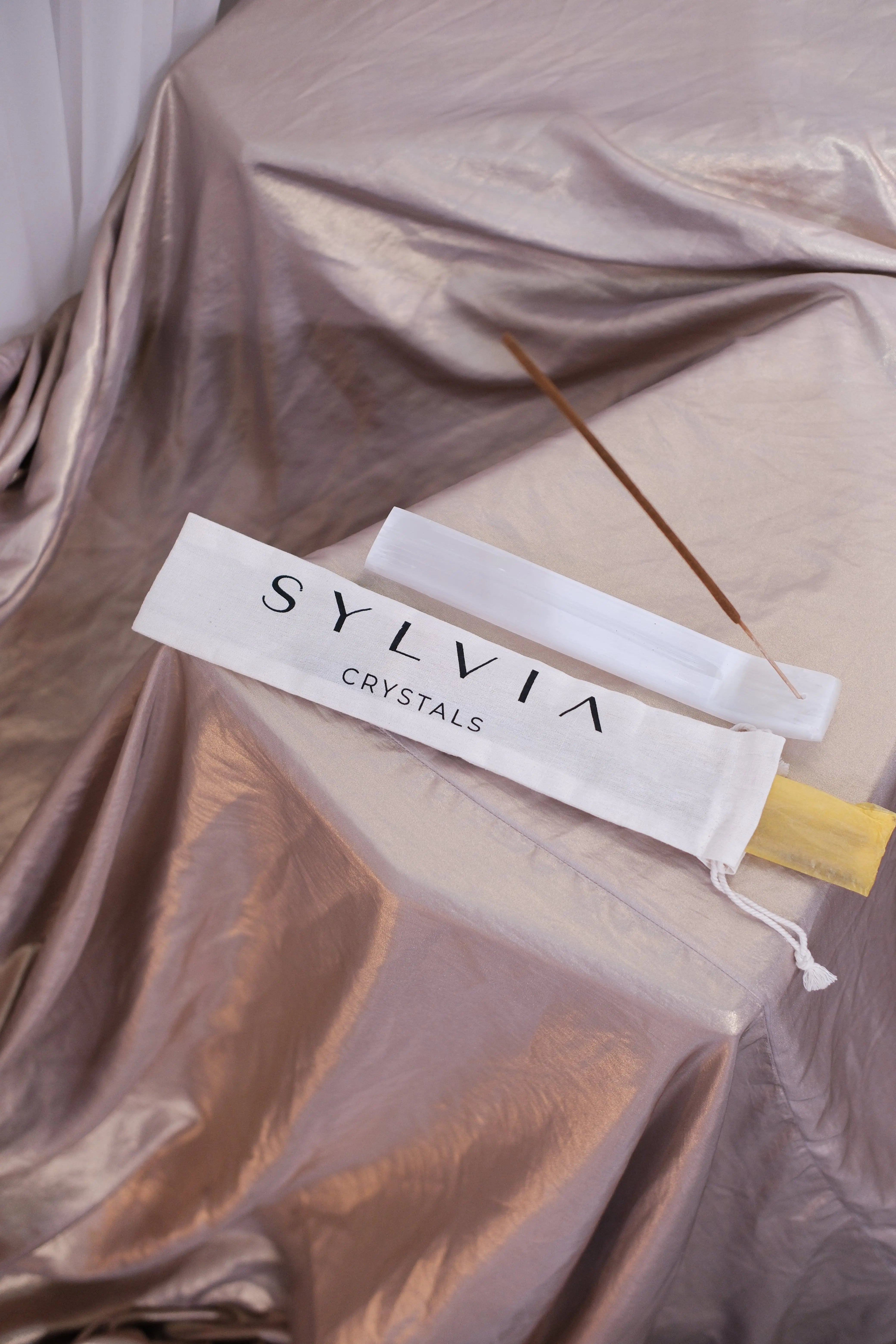 Elegant display of incense sticks on silk, featuring a white pouch labeled 'Sylvia Crystals'.