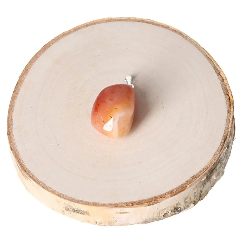 Banded Carnelian Tumbled Pendant showcasing unique banding on a natural wood base, highlighting its polished finish and vibrant energy.