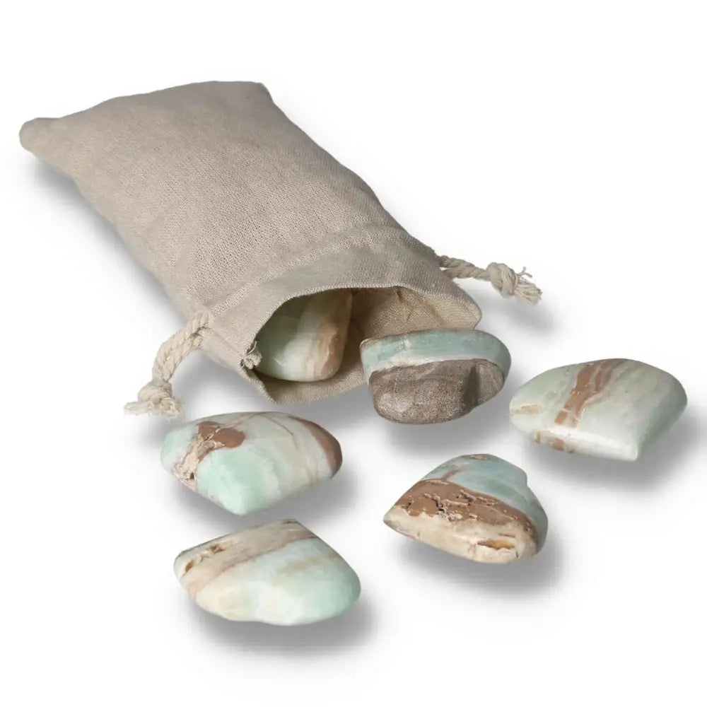 Caribbean Calcite Heart S stones spilling from beige pouch, showcasing unique blue and white hues by Sylvia Crystals for peace and balance.