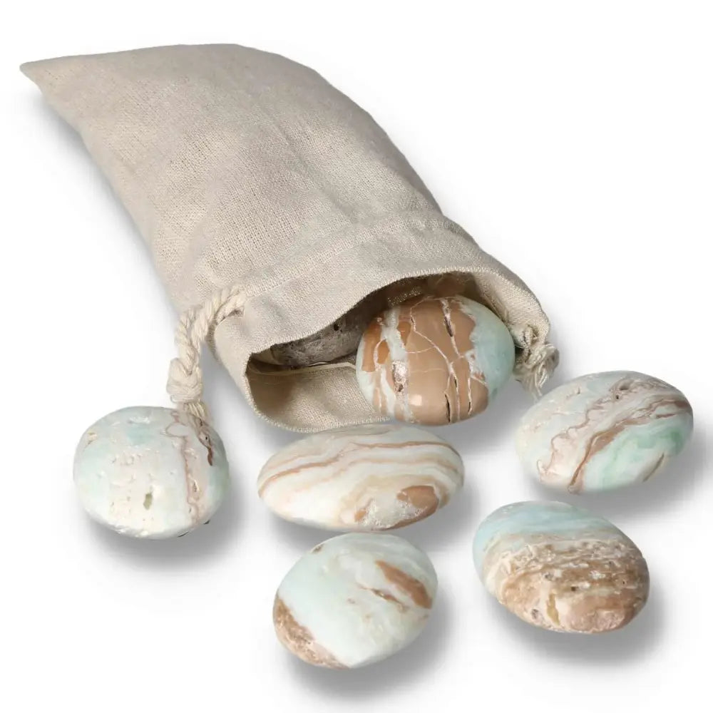 Caribbean Calcite palm stones spilling from a linen pouch, showcasing calming blue and creamy white swirls, promoting meditation and balance.