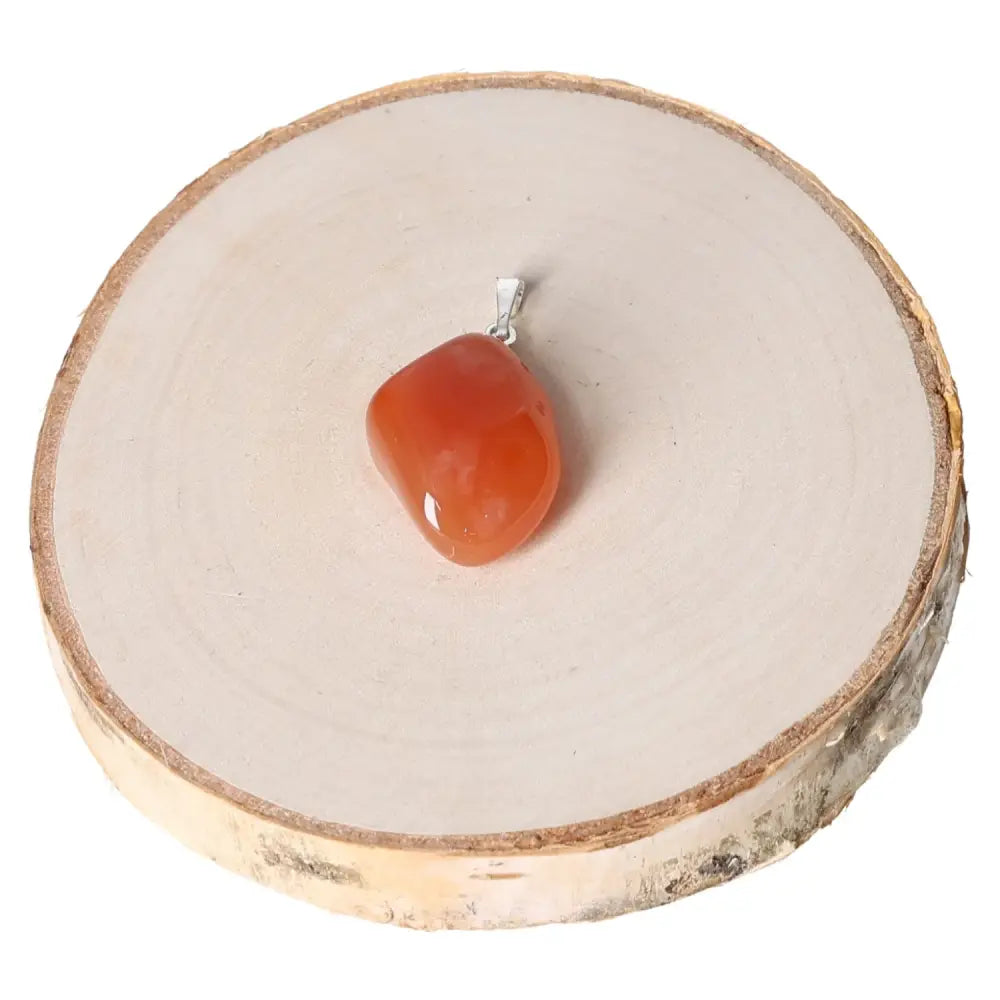 Carnelian Botswana Tumbled Pendant on wooden display; showcases vibrant hues and captivating patterns in a sophisticated setting.