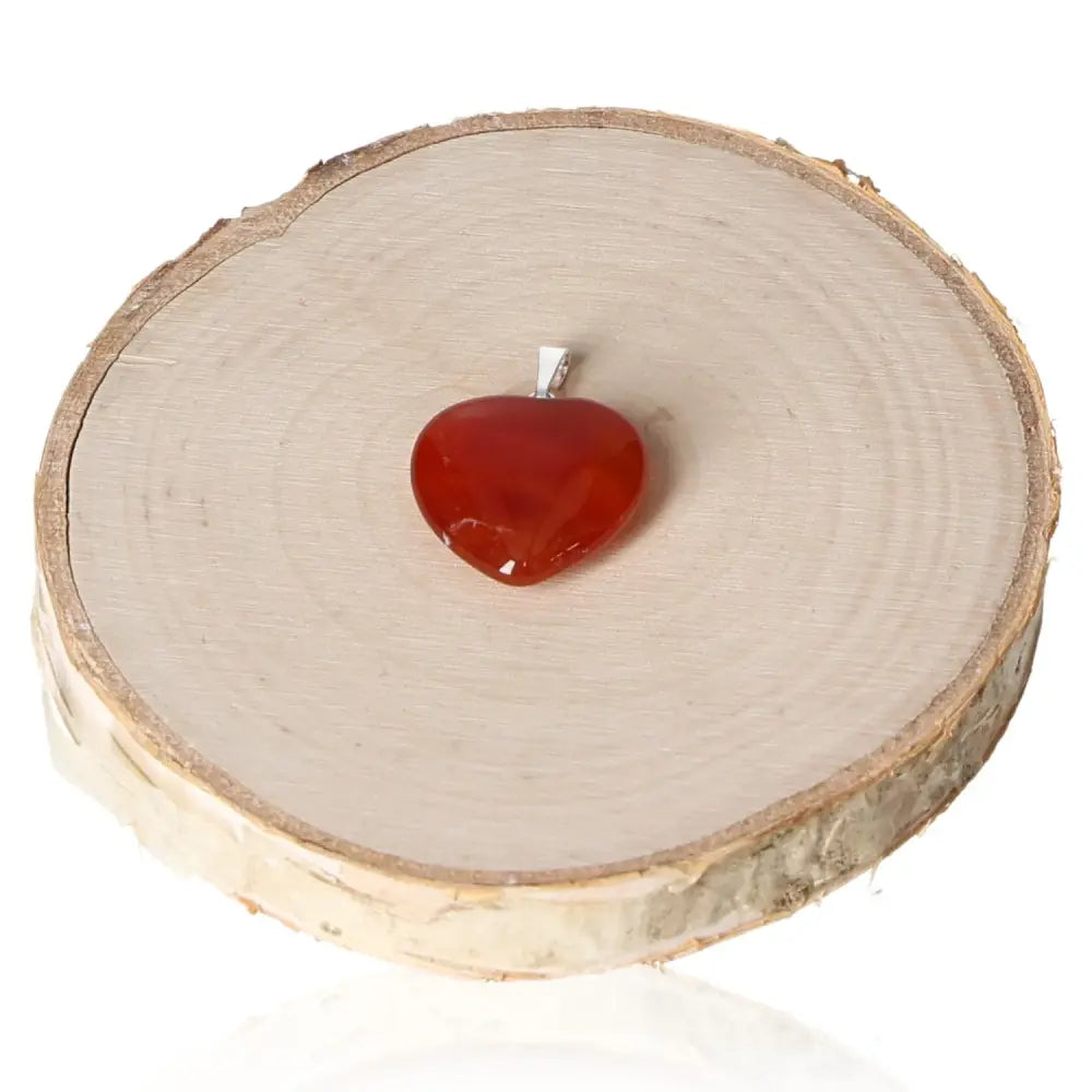 Carnelian Heart Pendant 20mm on wooden display, symbolizing love and passion with vibrant fiery hues for motivation and endurance.