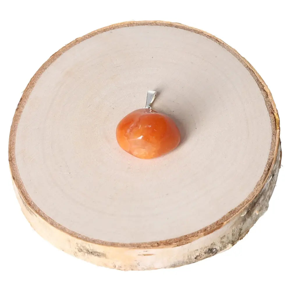 Carnelian tumbled pendant on wood slice, showcasing its polished orange and red hues, symbolizing passion and creativity.