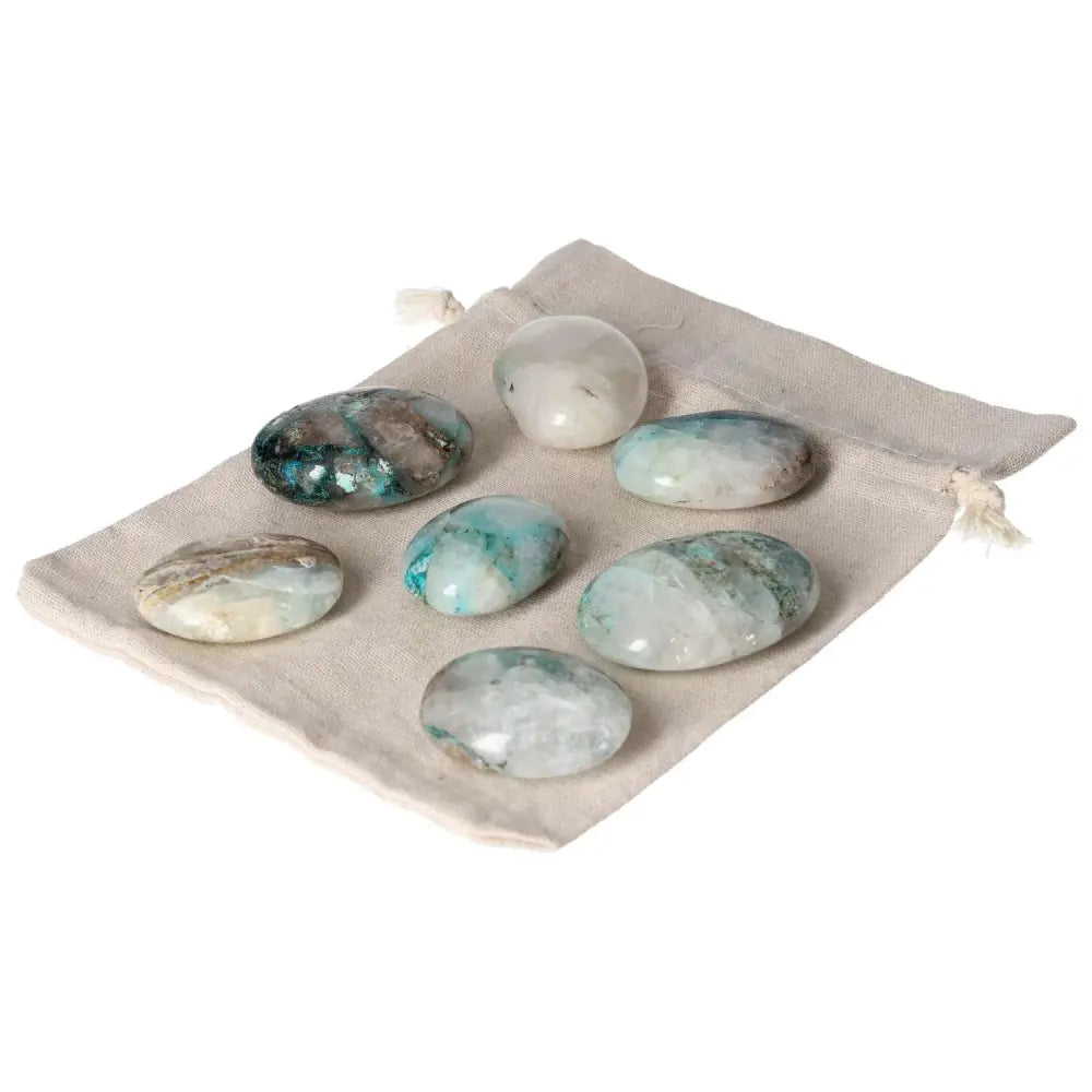 Chrysocolla palmstones on a beige drawstring pouch, showcasing their calming blue-green hues and smooth polished surfaces.