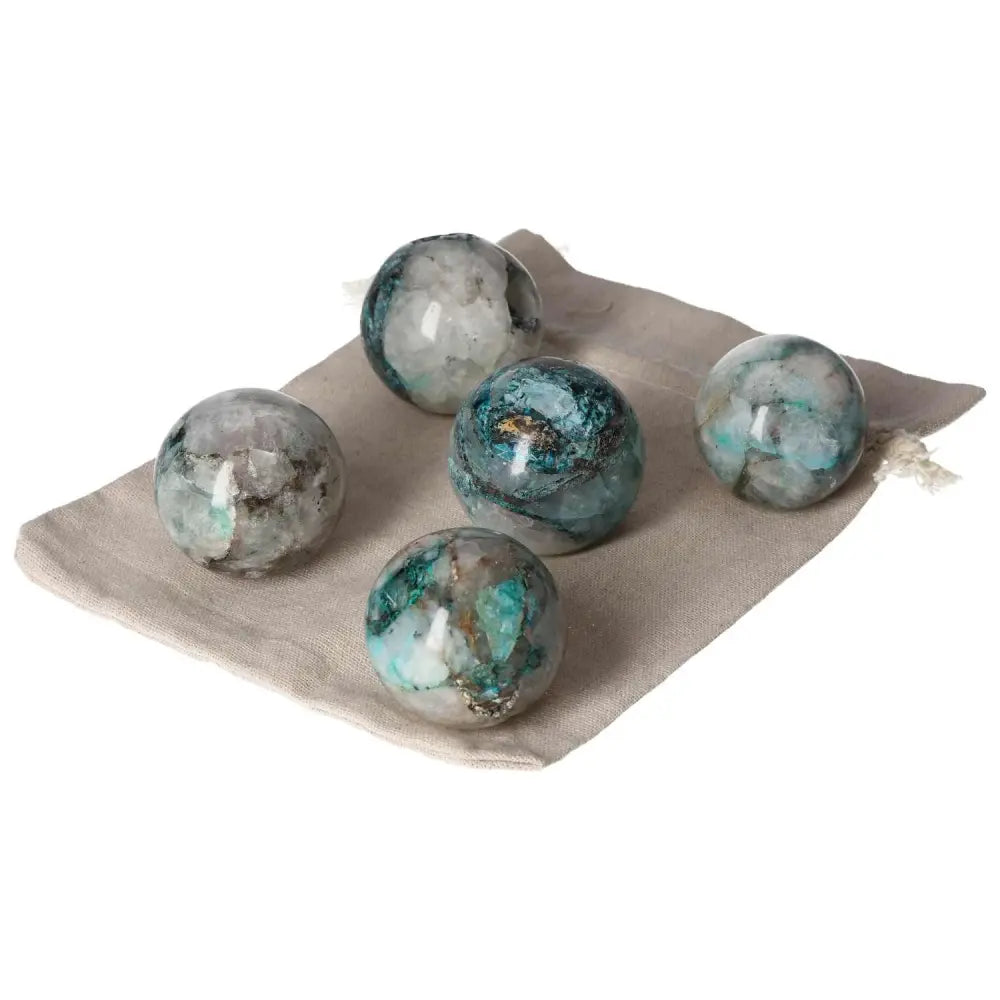 Five chrysocolla spheres with blue-green hues on a beige cloth, symbolizing communication and feminine energy.