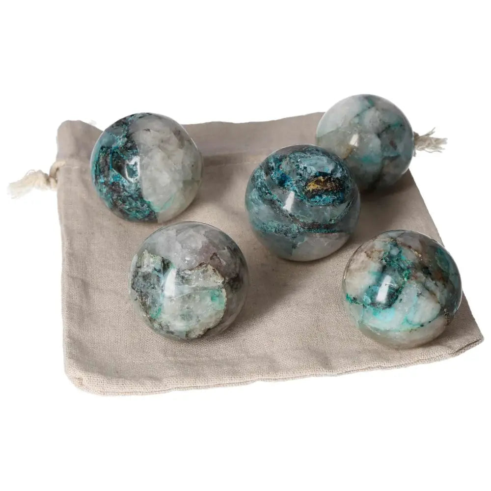 Five chrysocolla spheres on a natural fabric pouch, showcasing their unique blue-green hues and swirling patterns.