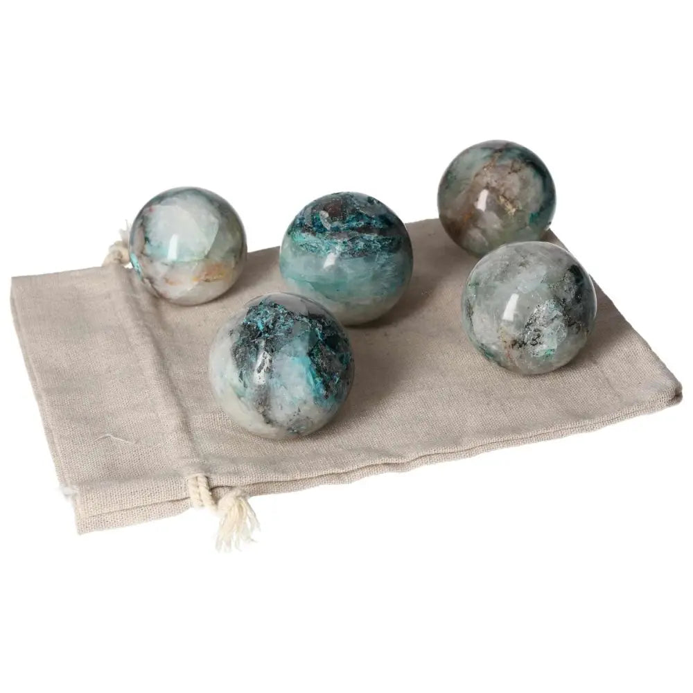 Set of polished chrysocolla spheres on a beige cloth, showcasing their blue-green hues and powerful feminine energy properties.