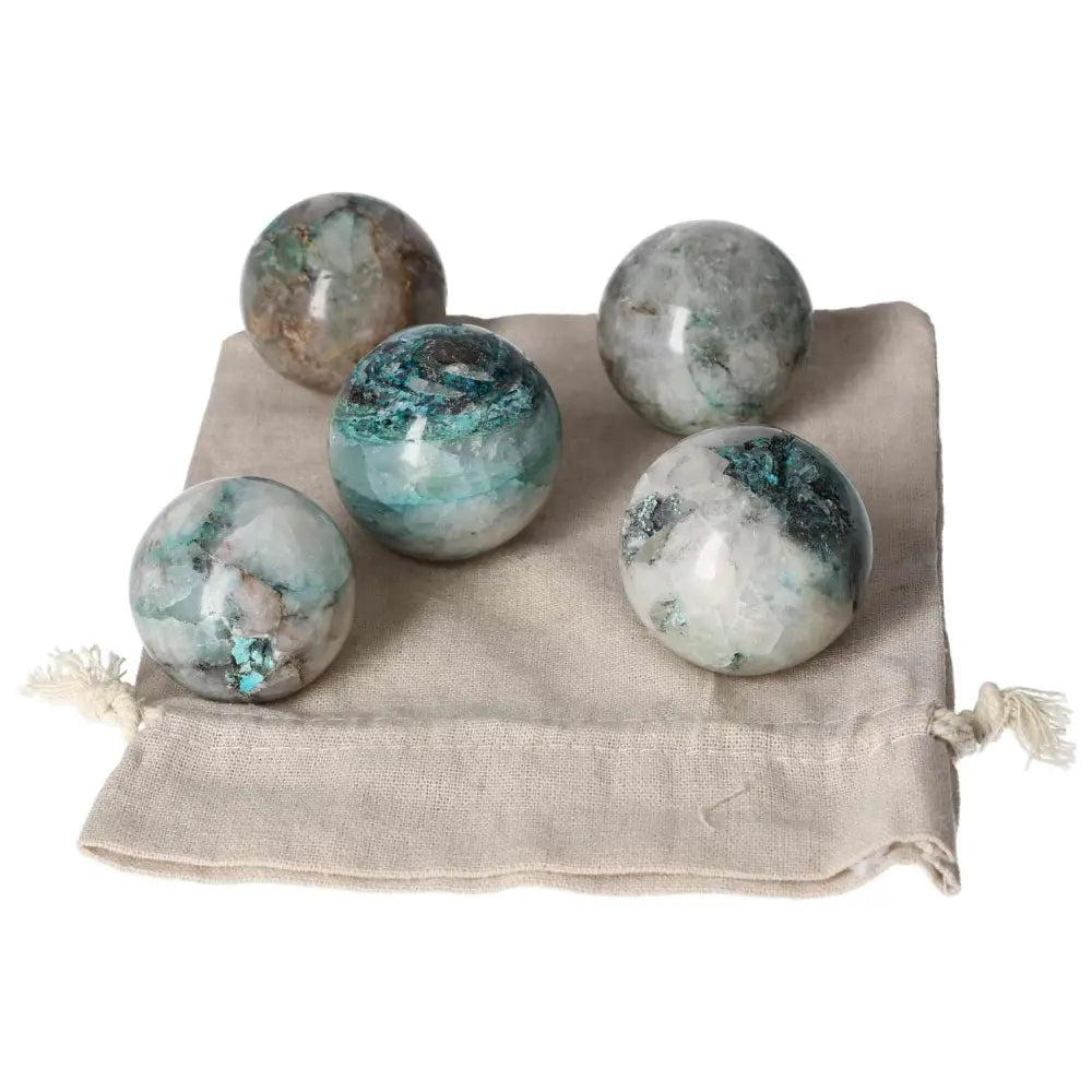 Five Chrysocolla spheres resting on a beige drawstring pouch, showcasing vibrant blue and green hues, ideal for enhancing communication skills.