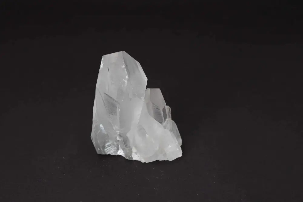 Clear Quartz Cluster on a dark background, showcasing multiple crystal points and radiant clarity. Ideal for energy amplification and purity.