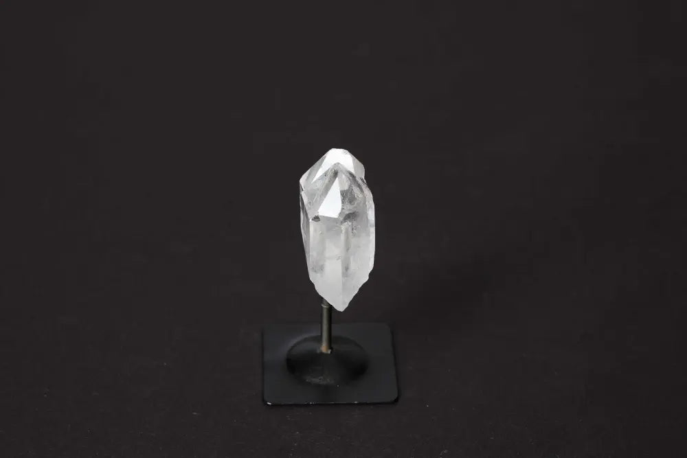 Clear quartz crystal on metal stand, showcasing its unique properties and association with chakras and zodiac signs.