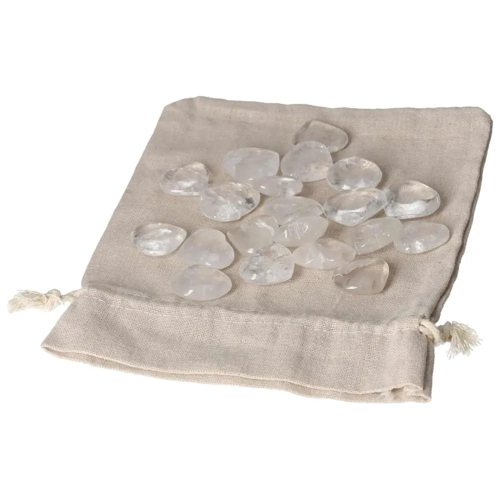 Clear Quartz small heart stones on a beige drawstring bag, known for purification and energy harmonizing properties.
