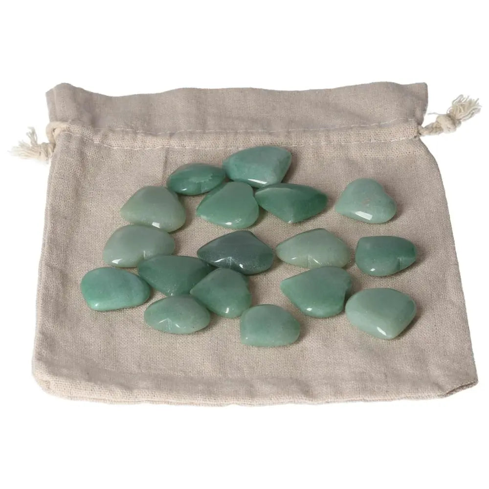 Collection of small green aventurine hearts on a beige cloth, promoting luck, prosperity, and inner peace through calming properties.