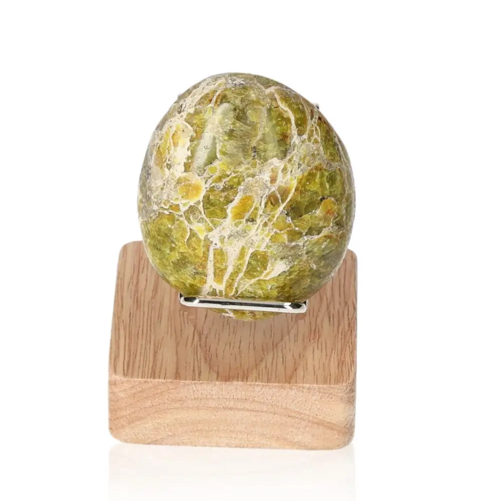 Green Jasper Palmstone by Sylvia Crystals on wooden stand, known for fostering tranquility and spiritual growth.