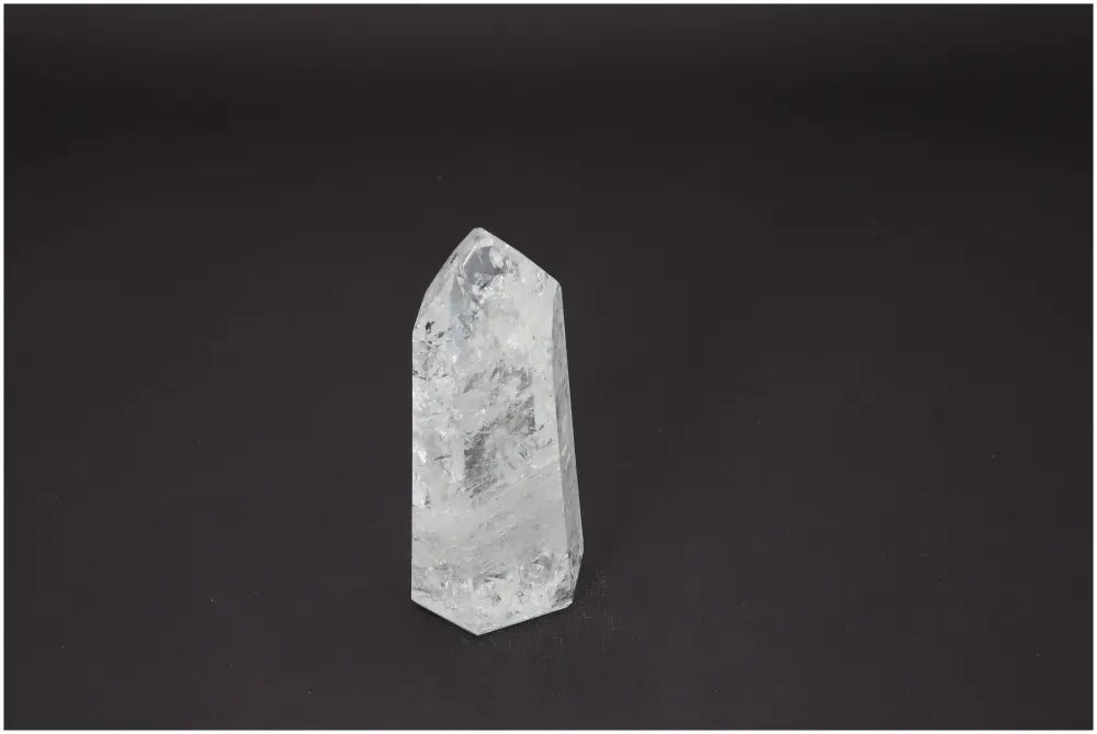 Clear Lemurian Quartz Obelisk standing against a dark background, known for its energetic and spiritual chakra properties.