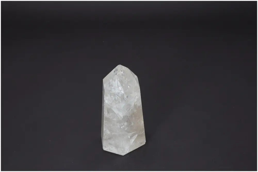 Clear Lemurian Quartz Obelisk with energetic and spiritual properties, linked to chakras and zodiac signs, on a dark background.