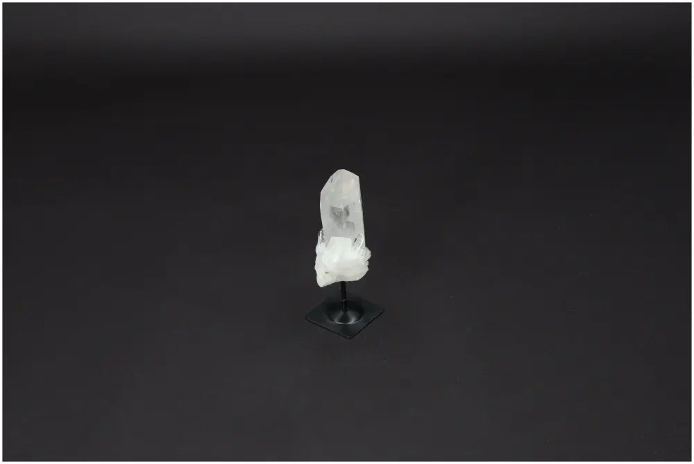 Clear Lemurian Quartz crystal on black metal stand against dark background, embodying clarity and balance.