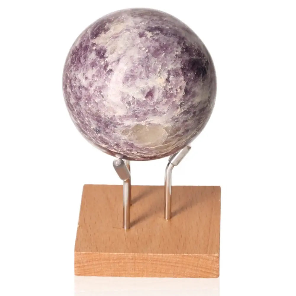 Lepidolite sphere on a wooden stand, promoting peace and emotional balance with soothing purple hues.