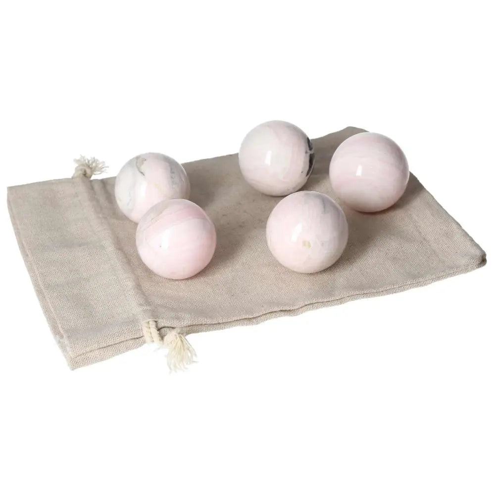 Five Manganocalcite spheres on a beige drawstring bag, promoting peace, creativity, and energy clearing.