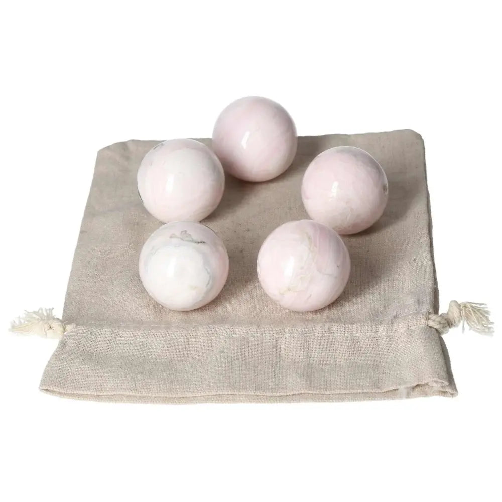 Five pink manganocalcite spheres on a beige cloth bag, promoting healing and creativity.