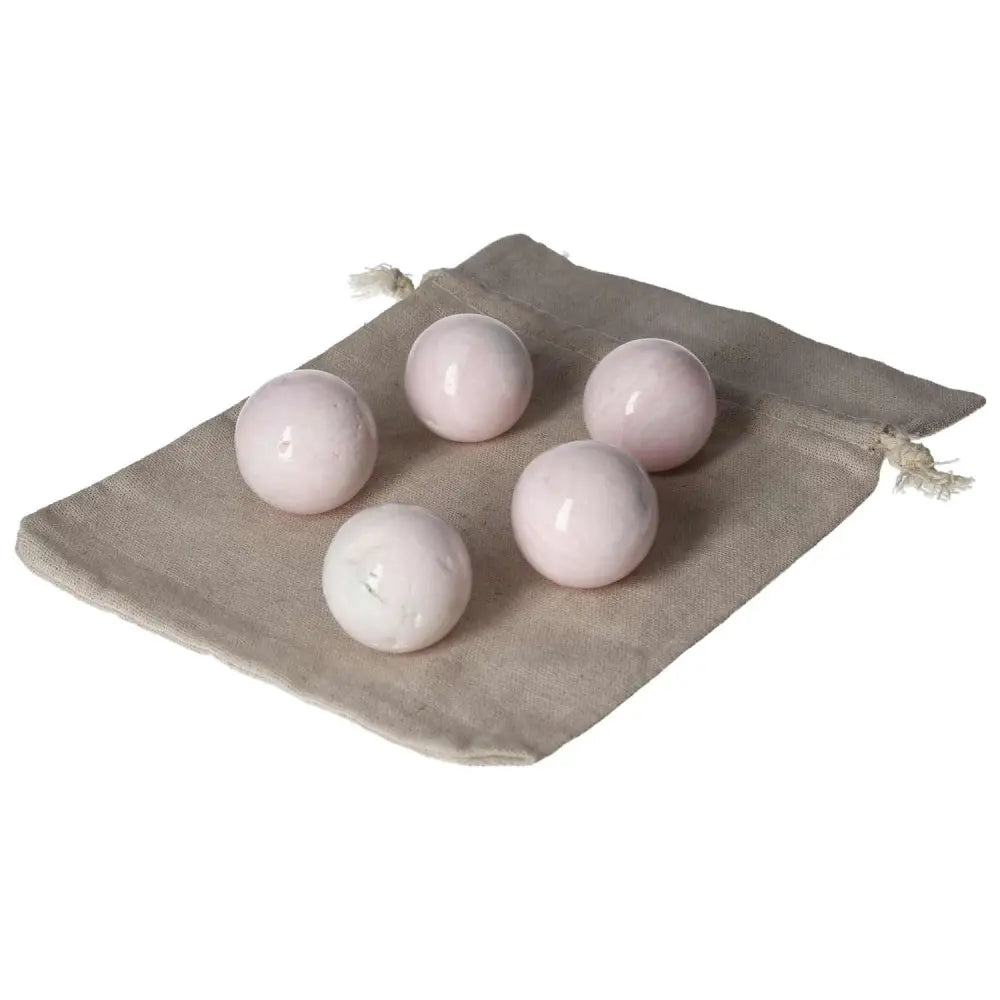 Five Manganocalcite spheres placed on a beige drawstring pouch, known for promoting peace, creativity, and clearing negative energy.