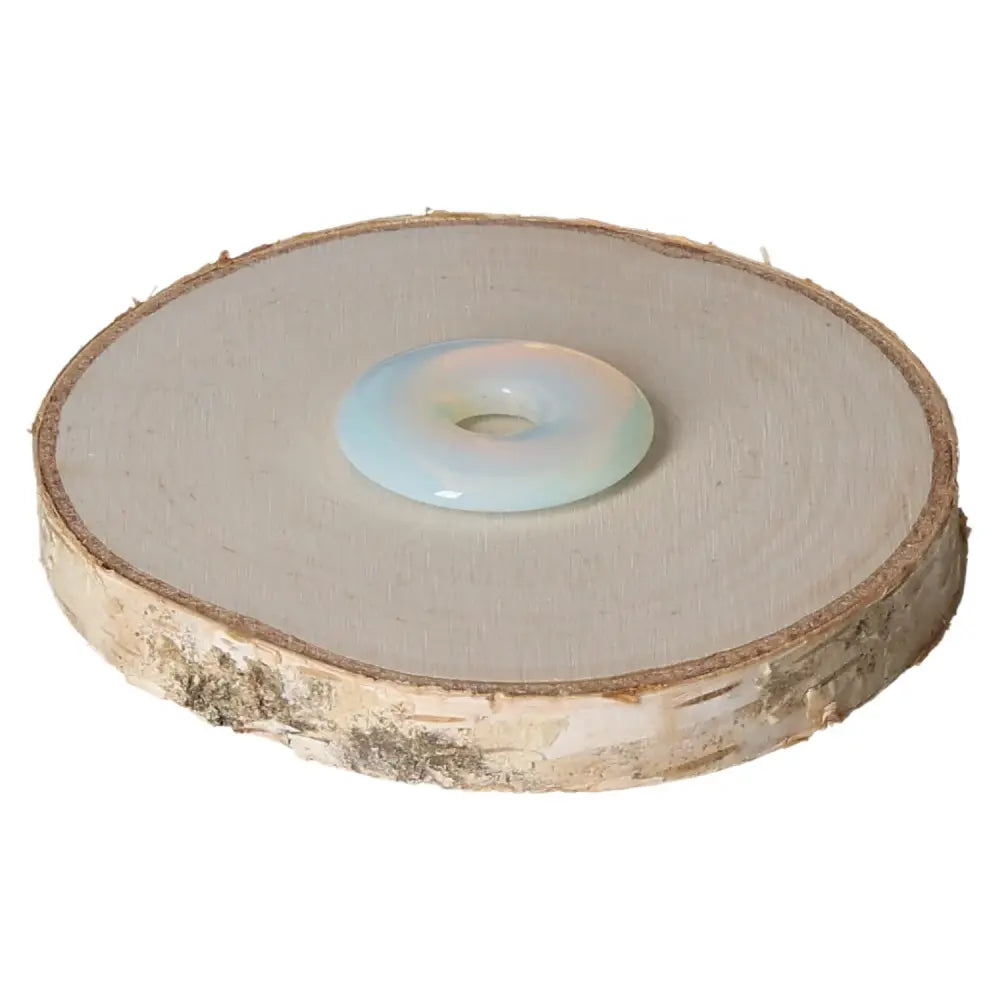 Opallite Donut 30mm by Sylvia Crystals on wood slice, showcasing its serene blue and white hues for spiritual resonance.
