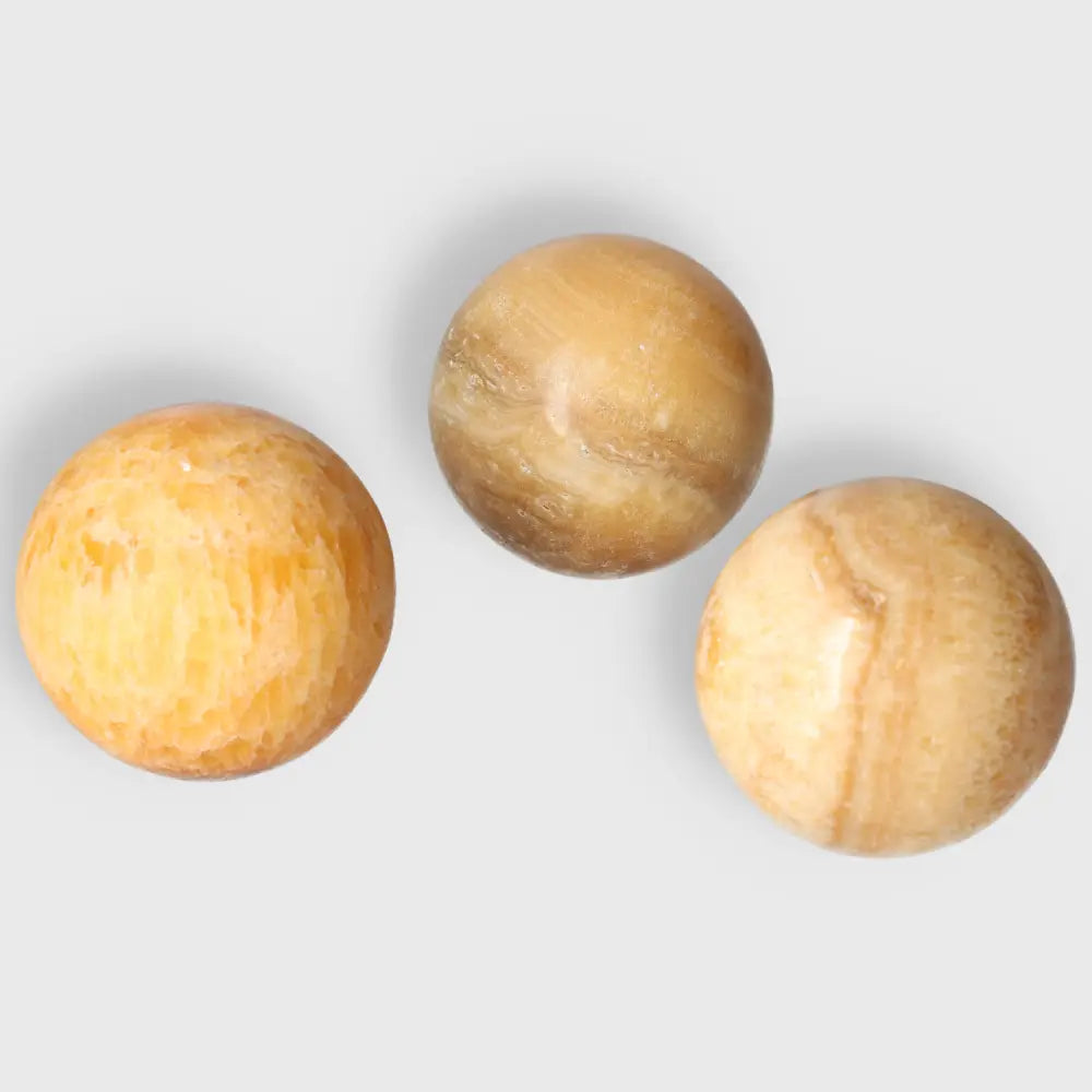 Three polished orange calcite spheres showcasing vibrant, warm colors and smooth, balanced shapes for positivity and creativity.