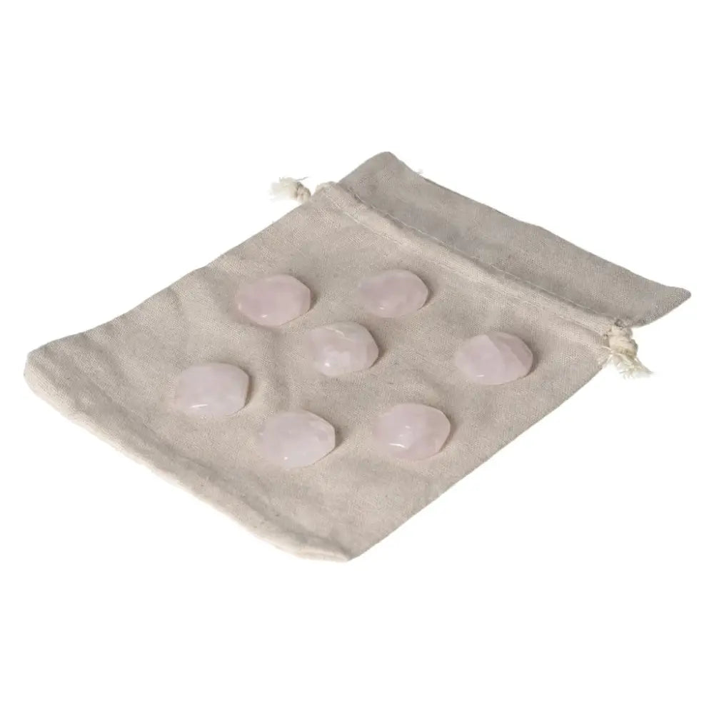 Seven small pink quartz palmstones on a beige fabric bag for emotional healing and heart chakra balance.