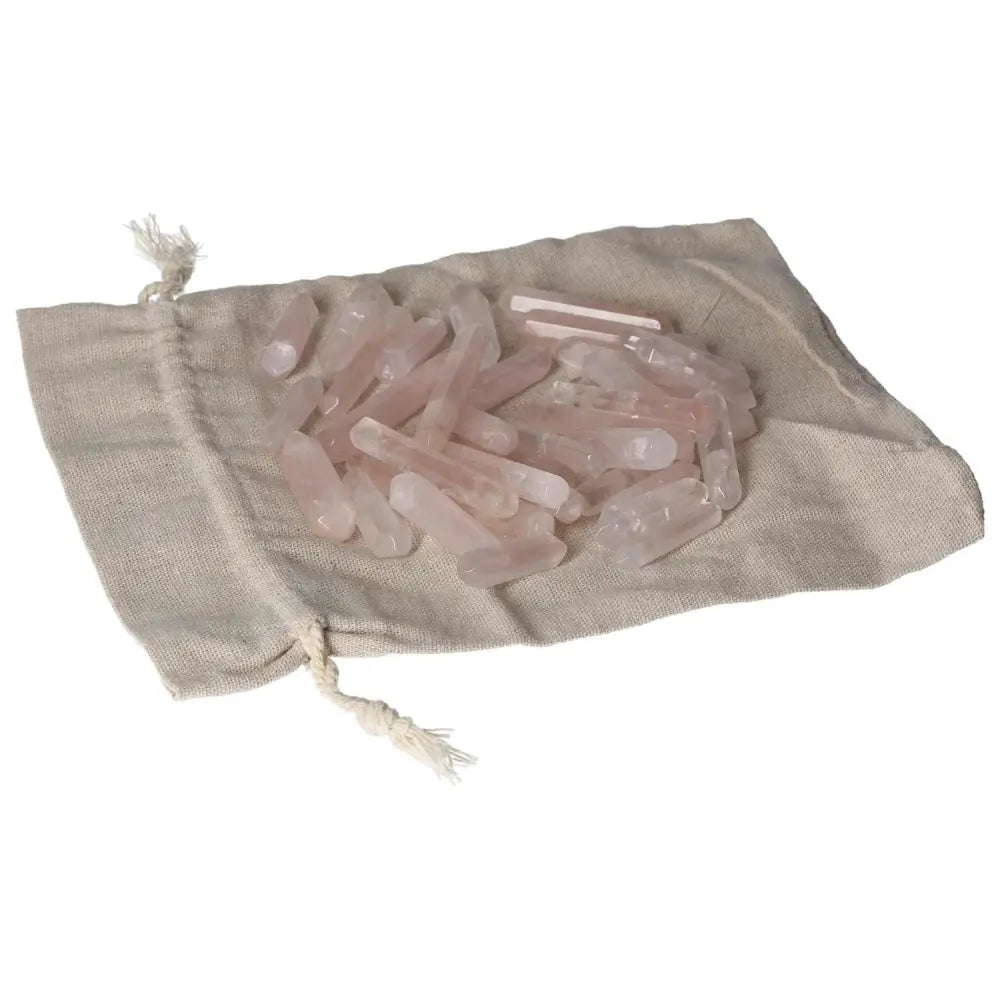 Pink quartz small sticks spilling from a beige linen pouch, showcasing the natural, translucent beauty of the crystals.