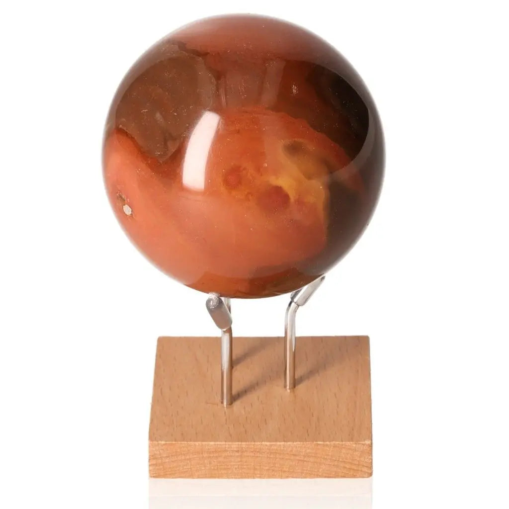 Polychrome Jasper Sphere with vibrant red, brown, and yellow hues on a wooden stand, known as Desert Jasper for its mosaic colors.