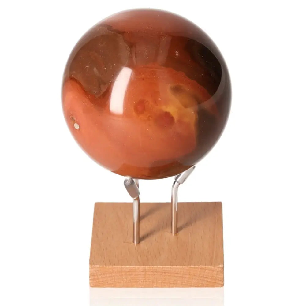 Polychrome Jasper Sphere displaying vibrant hues on a wooden stand, showcasing its unique banded patterns as a captivating centerpiece.