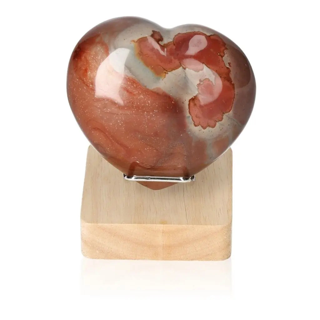 Heart-shaped Polychrome Jasper stone with vibrant red, brown, and orange hues, displayed on a wooden stand, showcasing its natural beauty.