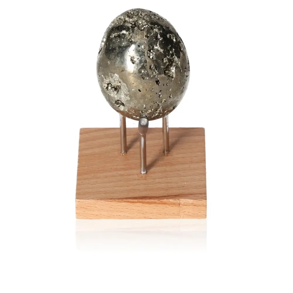 Pyrite egg with metallic luster displayed on a wooden stand, symbolizing abundance and prosperity.