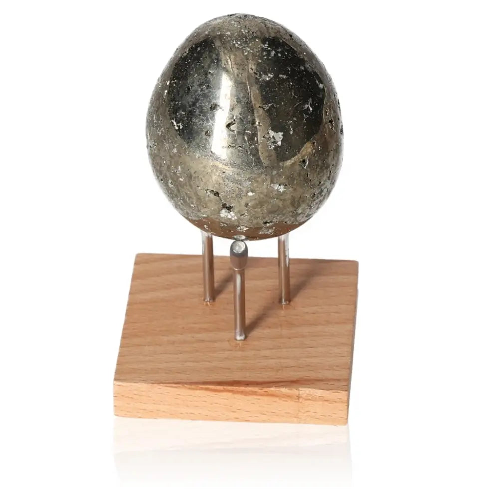Polished pyrite egg with metallic luster on a wooden stand, symbolizing wealth and success, often called "Fool's Gold."